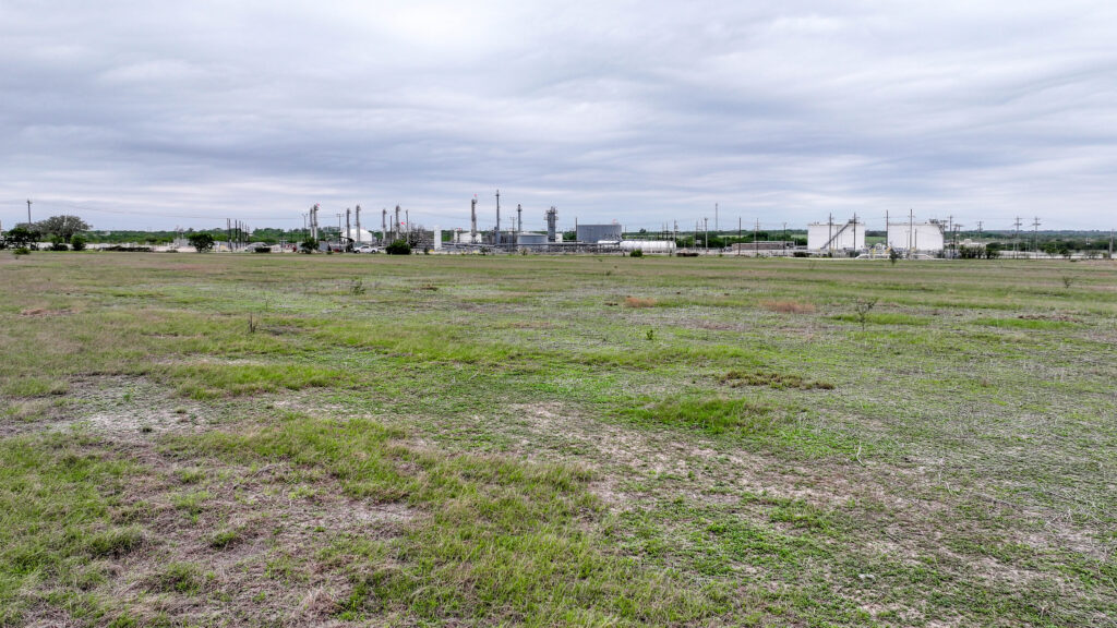 Open pasture on Three Rivers Development Tract with oilfield facilities in the distance